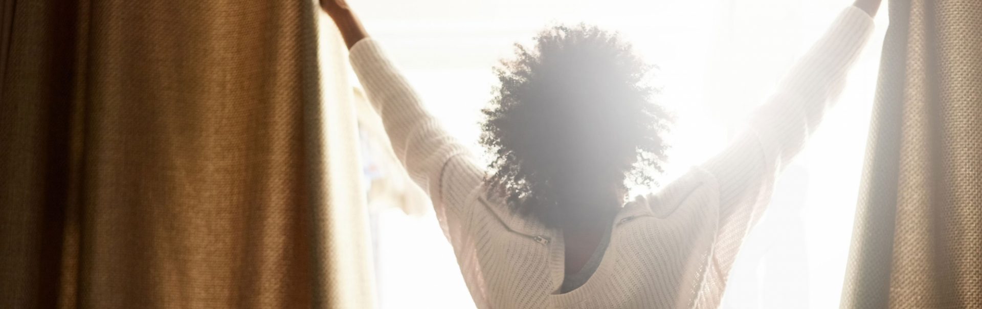 A women opening her curtain to let the sun shine into her room.