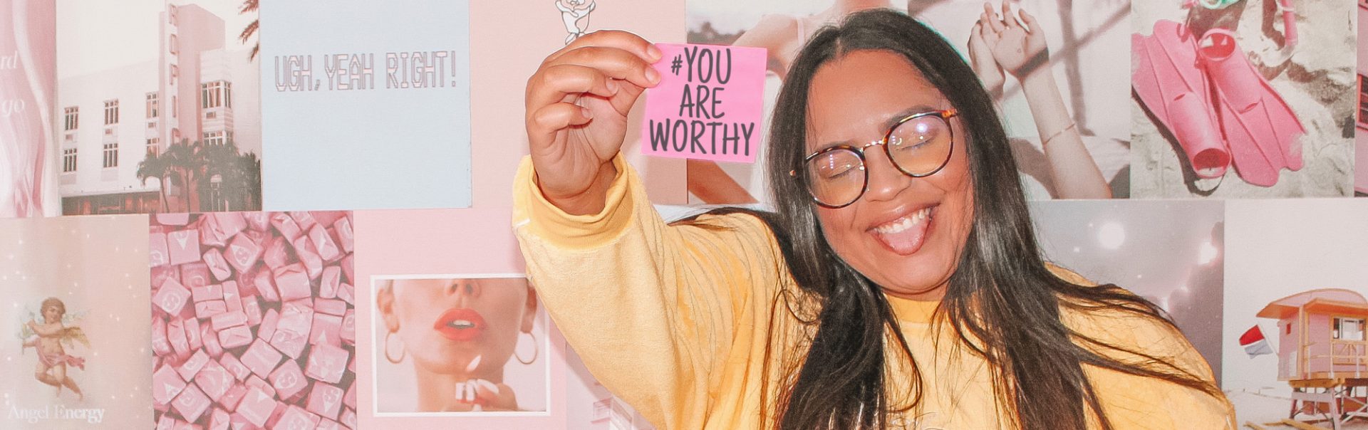 A women, smiling and holding a sign that says "You Are Worthy"