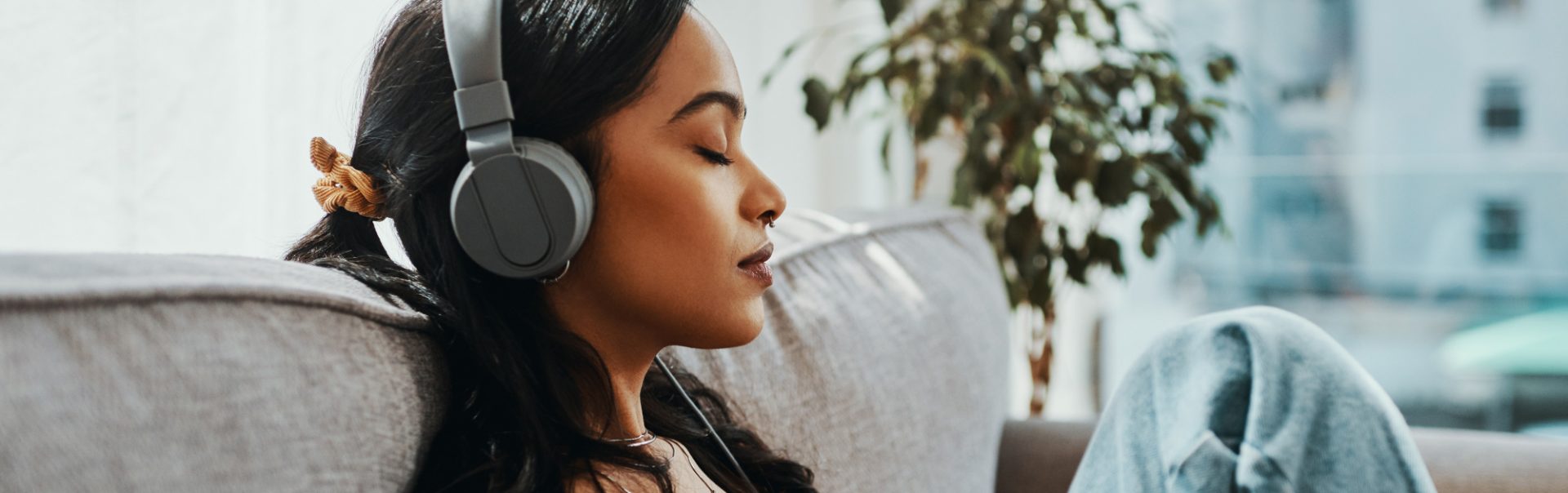 A woman closing her eyes and listening to headphones while sitting on the couch