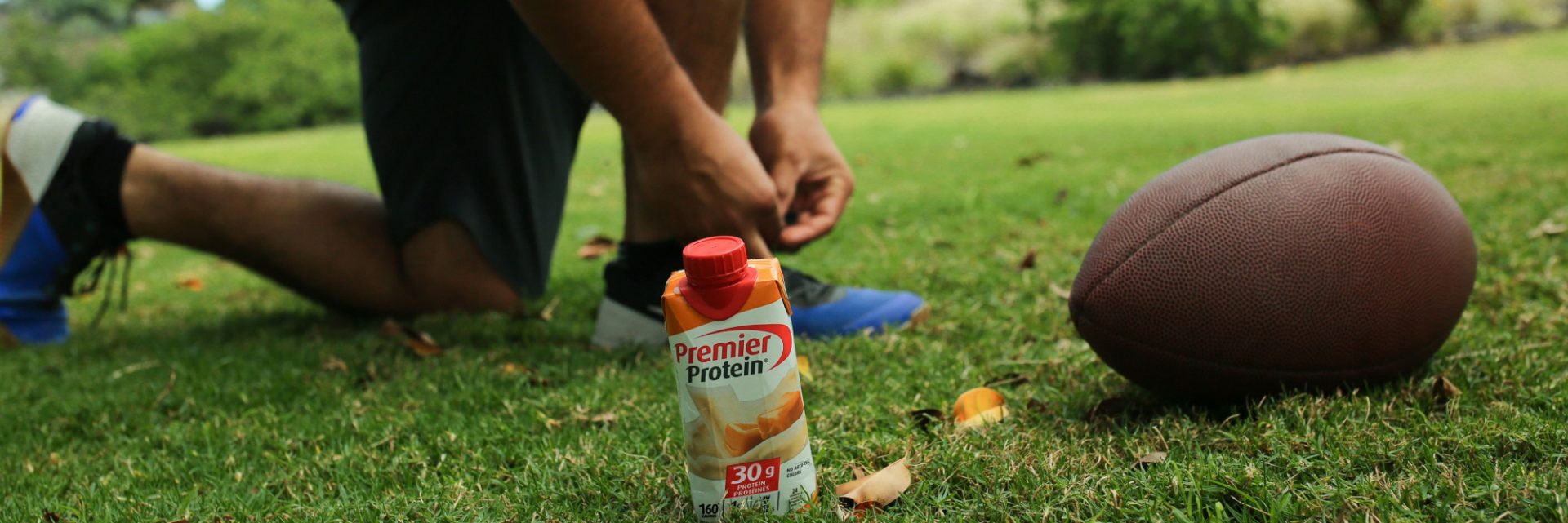 An athlete with a Premier Protein drink and a football.