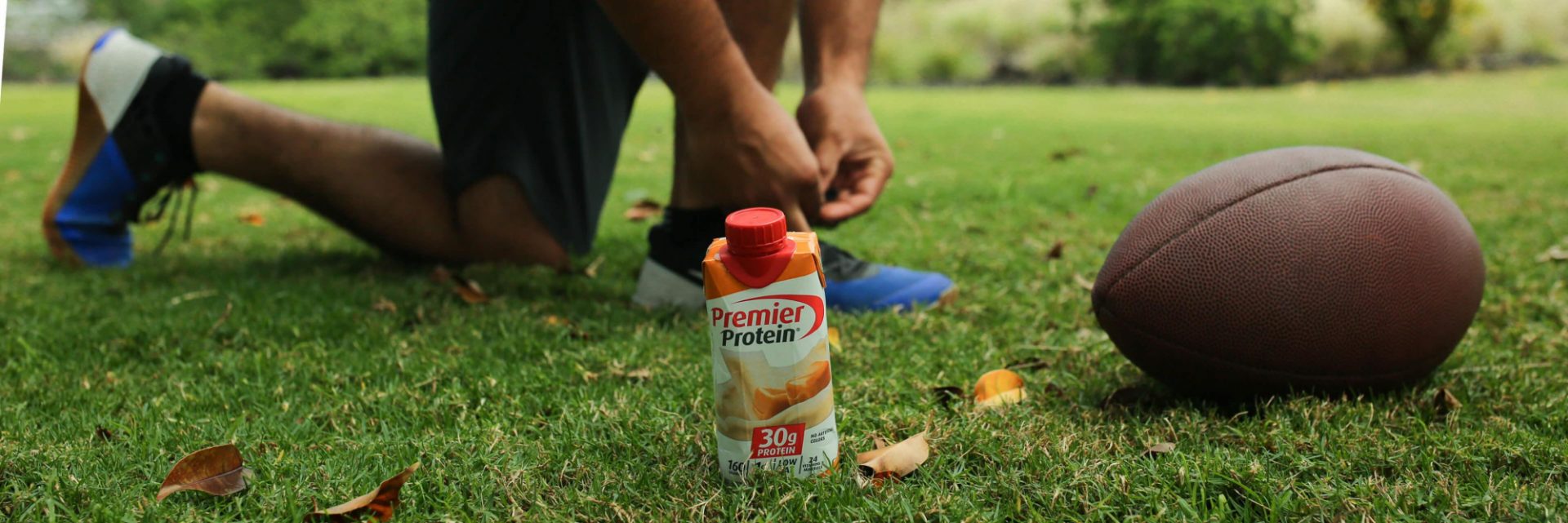 An athlete with a Premier Protein drink and a football.